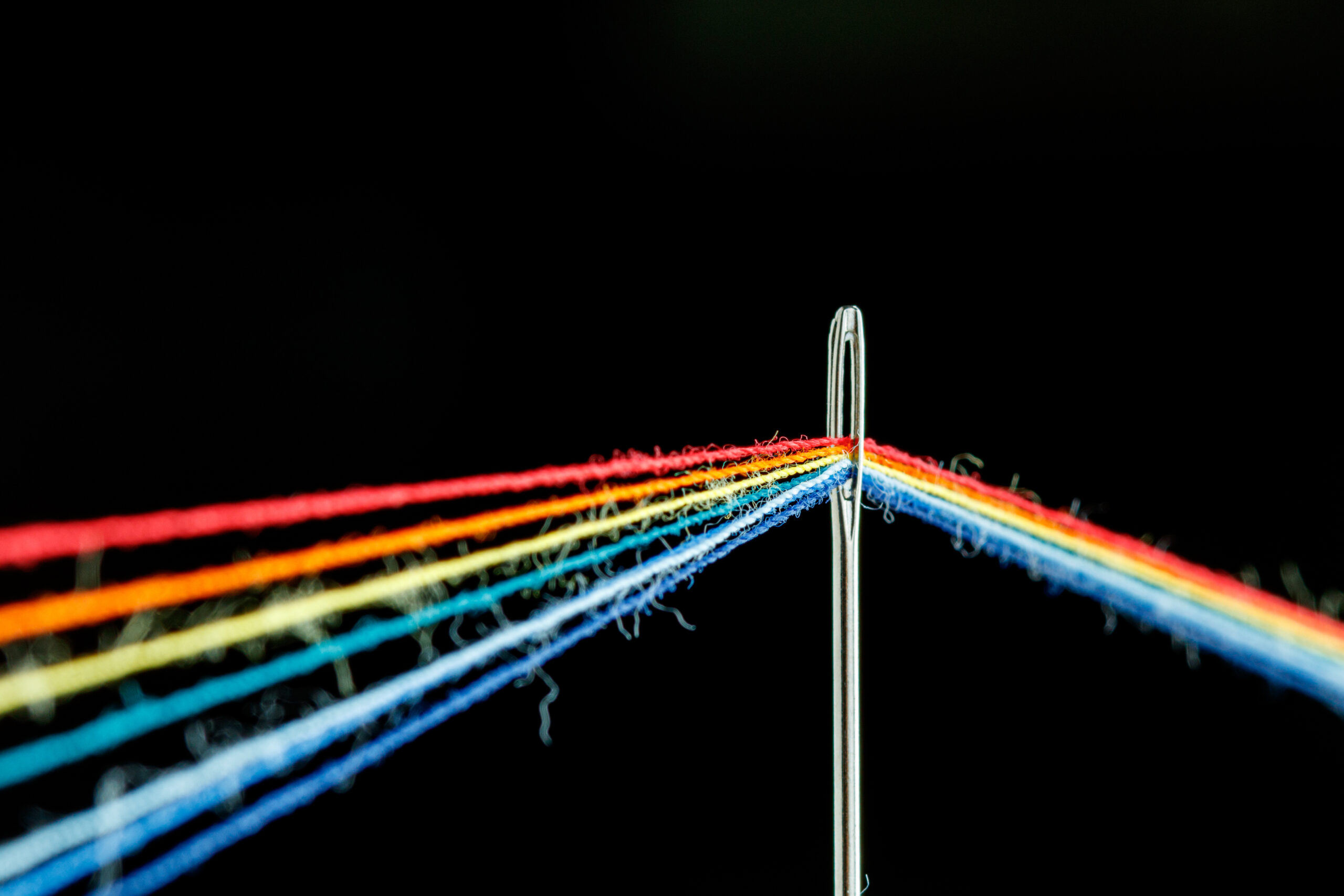 multi-colored threads for sewing in the form of a rainbow pass through an antique needle on a black background Vision